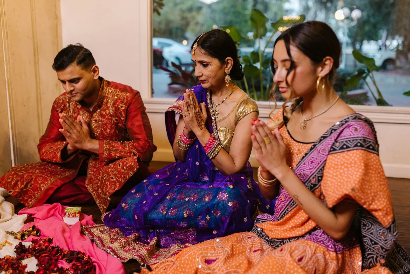 A family sitting indoors celebrating Diwali in colorful traditional clothing, hands in prayer.